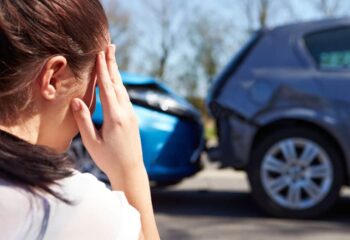 woman holding her head in pain after an injury with a car accident scene in the background