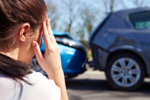 woman holding her head in pain after an injury with a car accident scene in the background