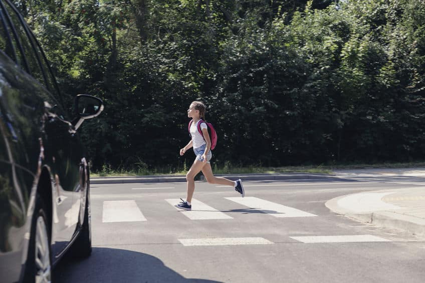 Girl wearing a backpack running through a pedestrian crossing in front of a car
