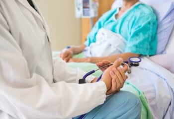 doctor sitting at a patient's bedside holding a stethoscope