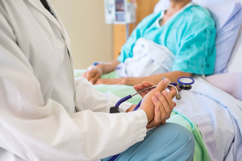 doctor sitting at a patient's bedside holding a stethoscope