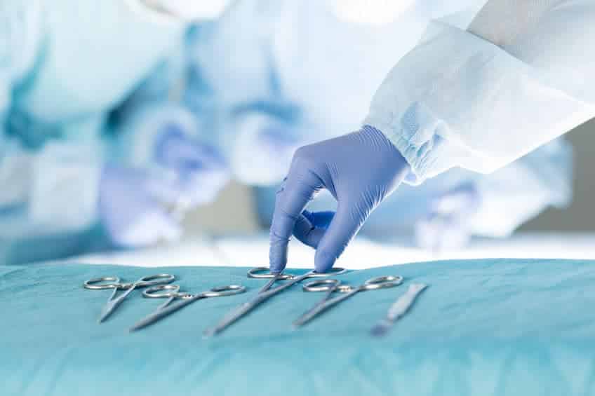 gloved hand selecting a medical instrument for surgeons working in the background
