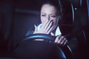 tired woman yawning while driving a car at night