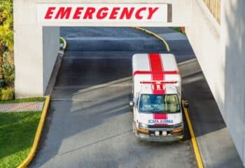 a view from the top of the entrance to the hospital and a modern ambulance with a red cross parked near the emergency entrance