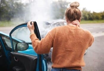 Rear View Of Female Driver With Neck Injury Getting Out Of Car After Crash