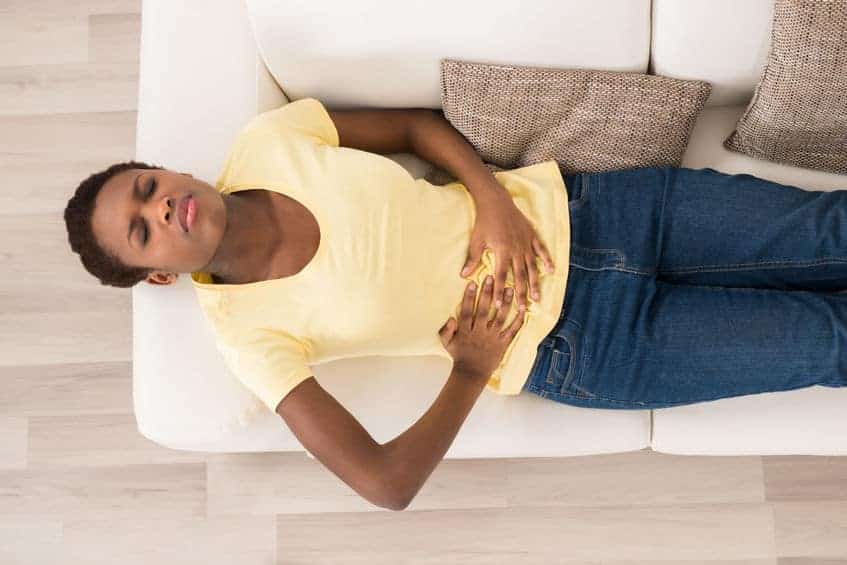 woman lying on couch clutching her stomach in pain