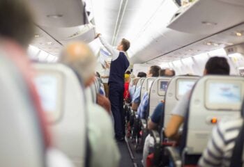 the interior of an airplane with passengers in seats and a flight attendant closing overhead luggage compartments