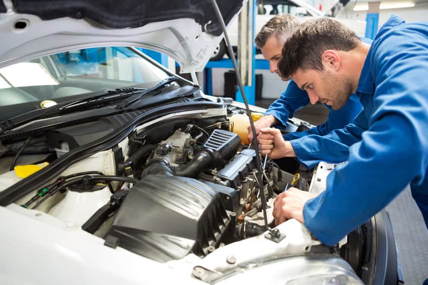 Two mechanics working together in a garage to repair a car after an accident