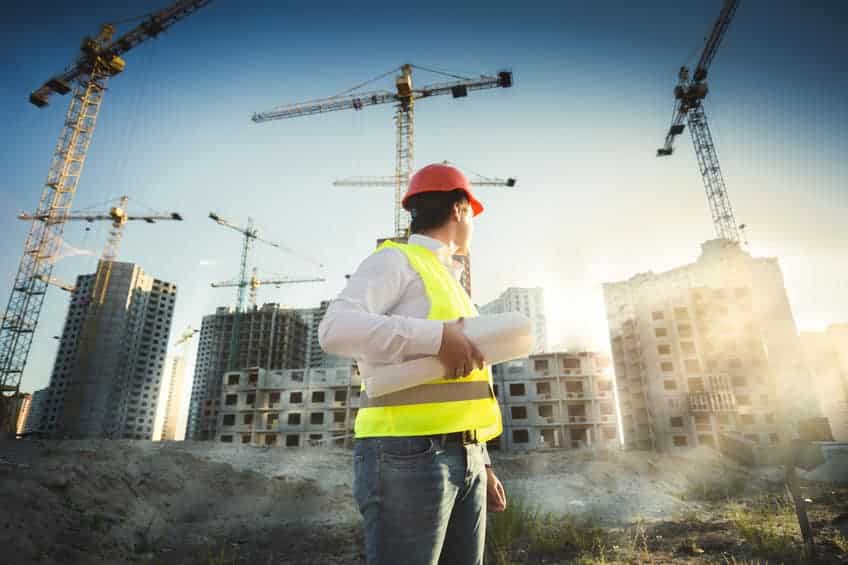 a construction worker in a hard hat looking back at a building site and cranes