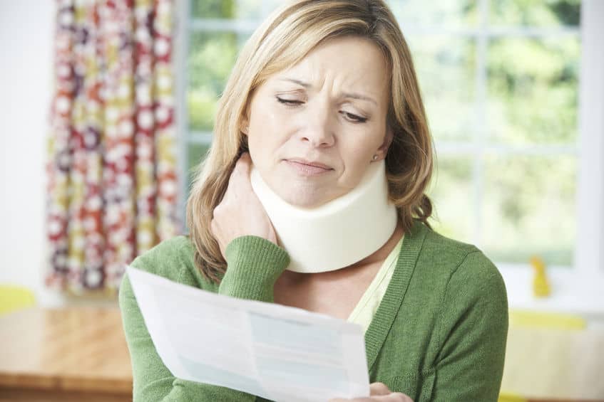 woman wearing a neck brace and wincing in pain while reading a letter from her car insurance