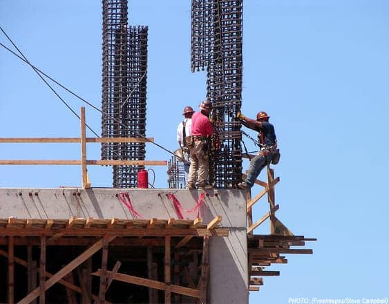 construction workers on the top of a building site, strapped into scaffolding for safety
