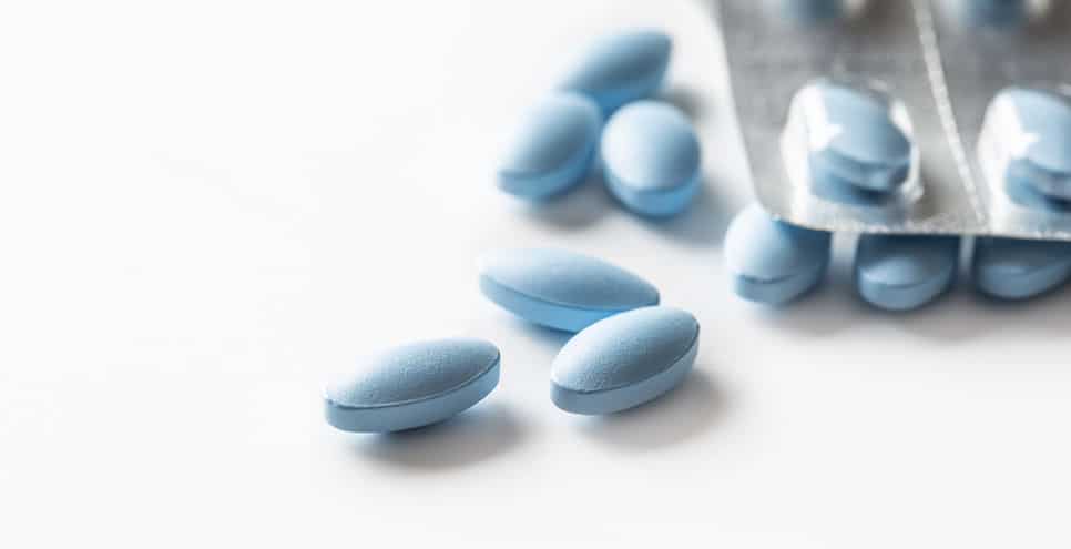 close up of blue pills lying loose on a white background with the same pills in blister packs behind them