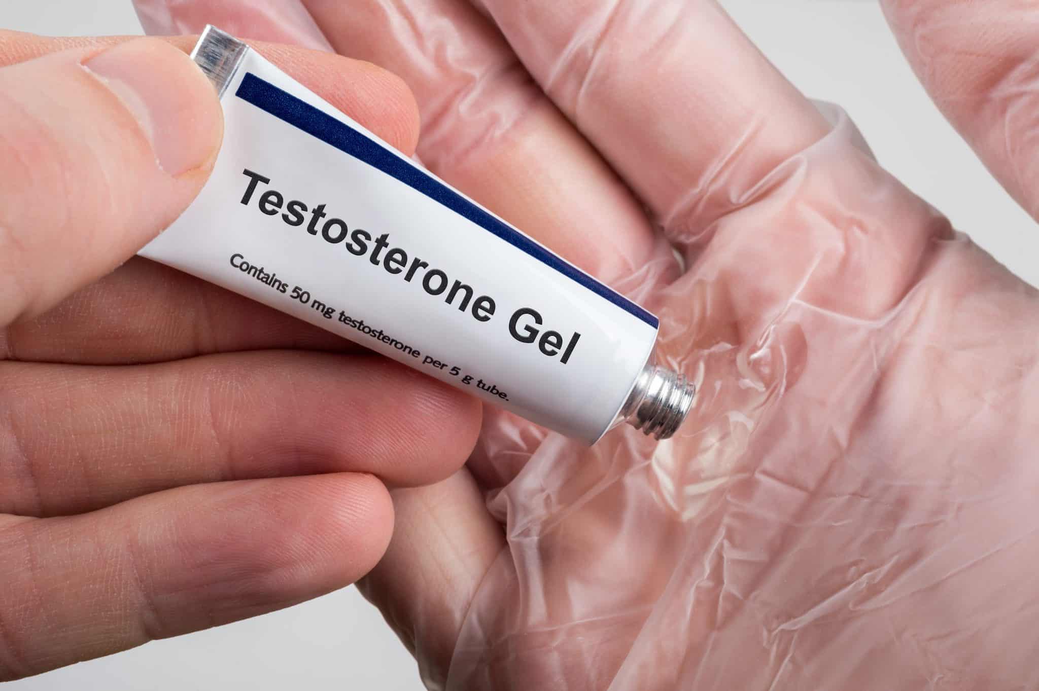 A mini container of testosterone gel being squeezed into a hand with a plastic glove on it. Testosterone Replacement Therapy (TRT) using testosterone gel.