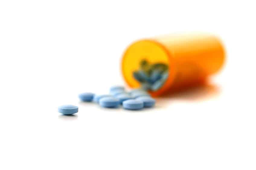 blue pills scattered on a table spilling out of a prescription bottle
