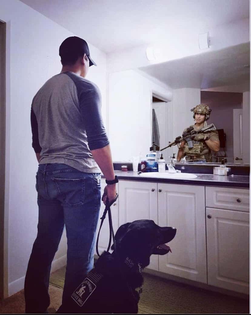 man looking in the mirror with his dog and the reflection shows the man in uniform