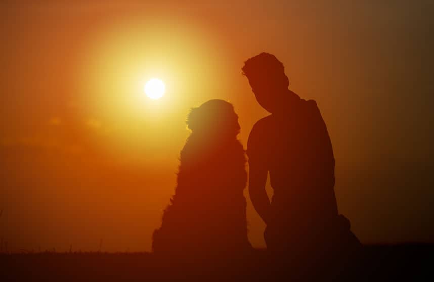 young man is sitting outside with his pet dog, on a summer evening, silhouetted by the sunset in the sky