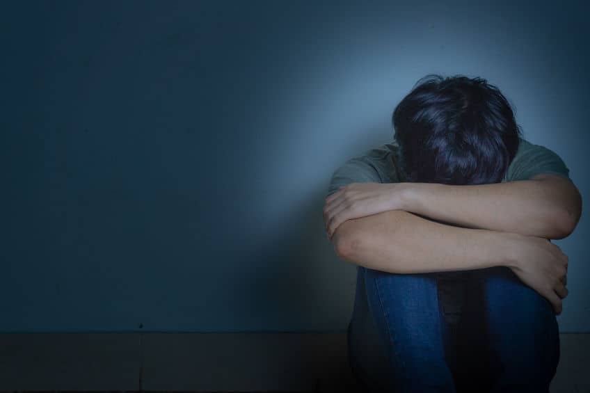 sad man hug his knee and cry sitting alone in a dark room