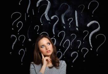 woman standing in front of a chalboard with question marks drawn in chalk around her head