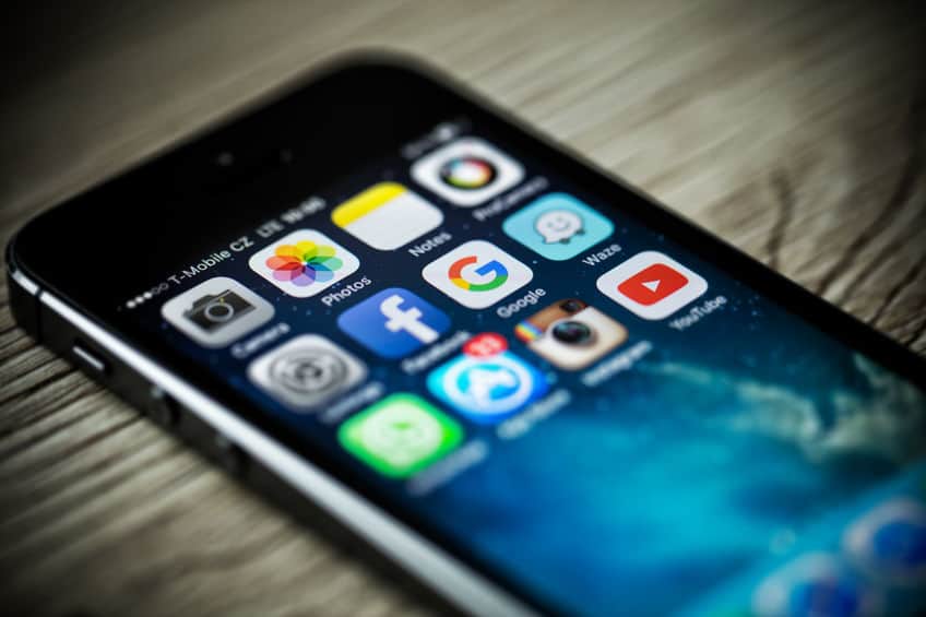 A close-up photo of Apple iPhone 5s start screen with apps icons. Popular social media icons on smart phone screen.