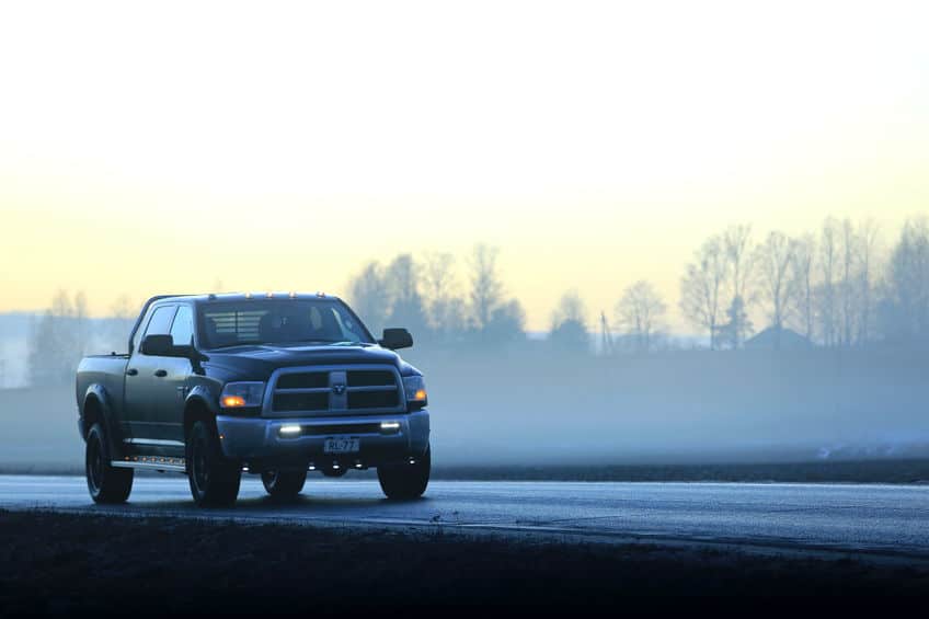 Dodge pickup truck moves along highway through fog at sunset time in winter.