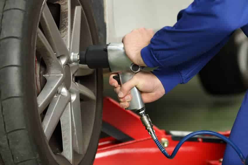 Close up of a car mechanic hands loosening wheel nuts with a pneumatic gun in a mechanical workshop