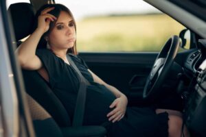 pregnant woman sitting in the drivers seat of a car after a car accident