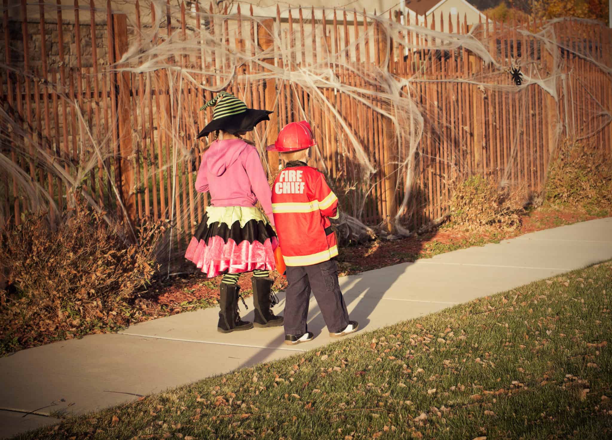 kids going trick or treating in a neighborhood, walking on the sidewalk in daylight, kids following safety measures