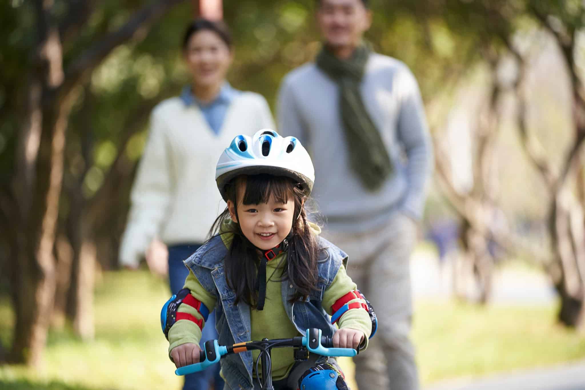 child riding a bicycle in a park with parents behind them